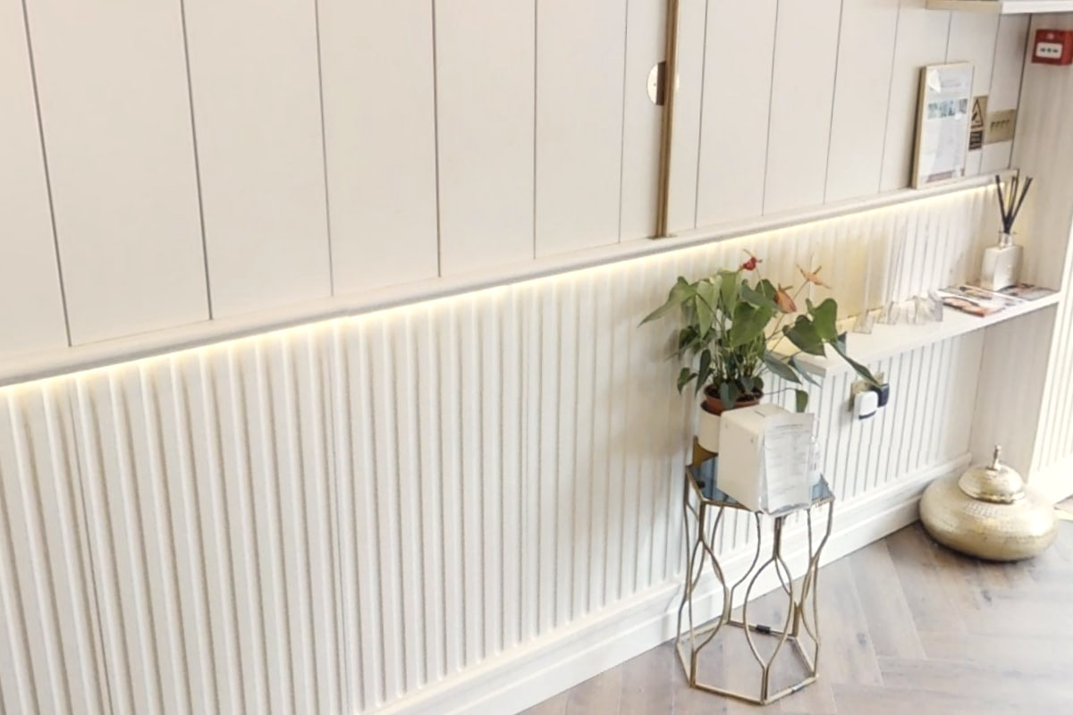 Fluted panelling lit by a warm strip light, with a plant on a brass stand, at Shirland Dental Practice
